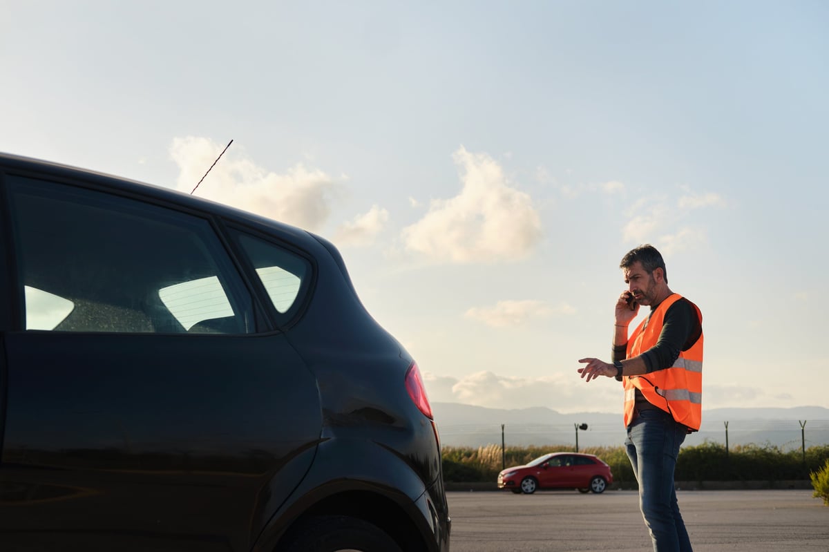 Driver waiting for a tow truck by a broken-down car at sunset