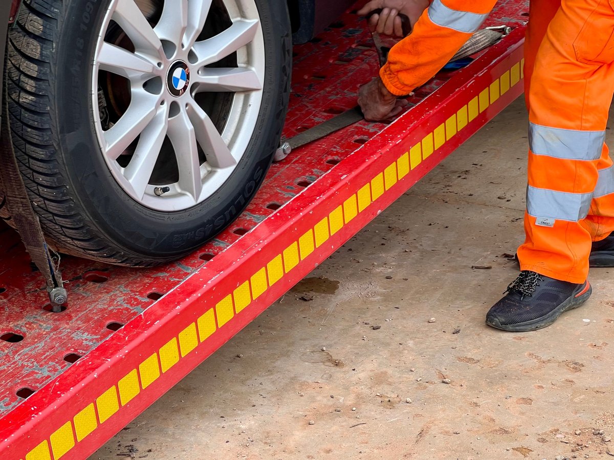 Service worker in high-visibility clothing securing a broken-down vehicle onto a recovery truck